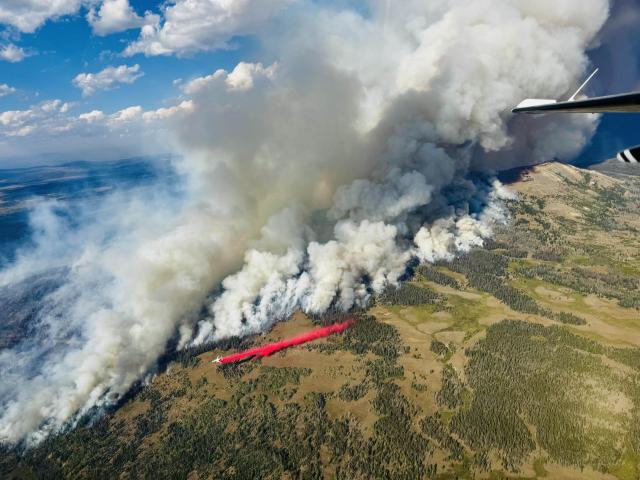 Aerial view of a fireline. Smoke billows as a plane drops retardant along the edge of the fire.