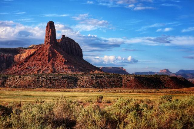 A spire of sandstone and adjoining cliffs stand tall above yellow grasses.