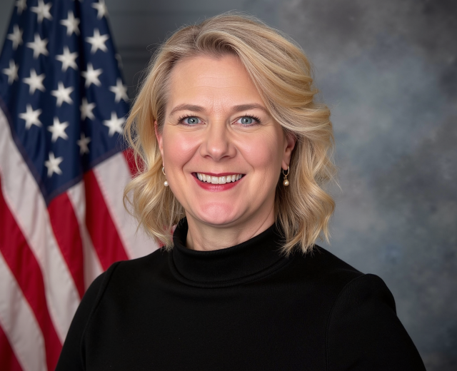 A portrait of Kim Okragly Prill in front of an American flag