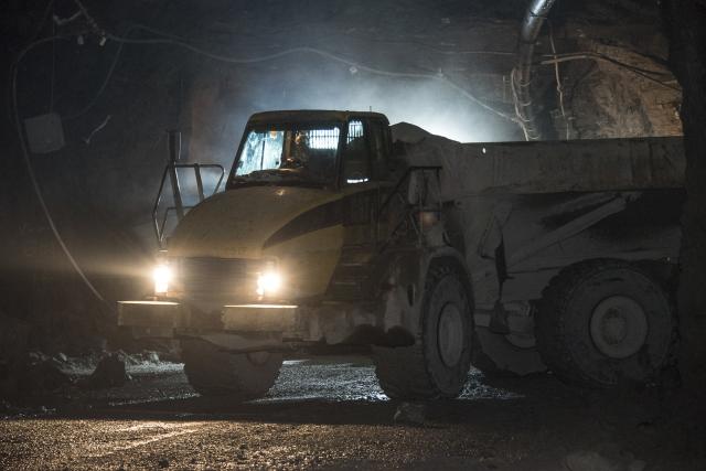 A large dump truck with its headlights on sits in a dark, subsurface mine