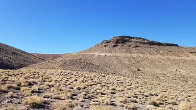 A hill in the high desert with yellow brush all around it.