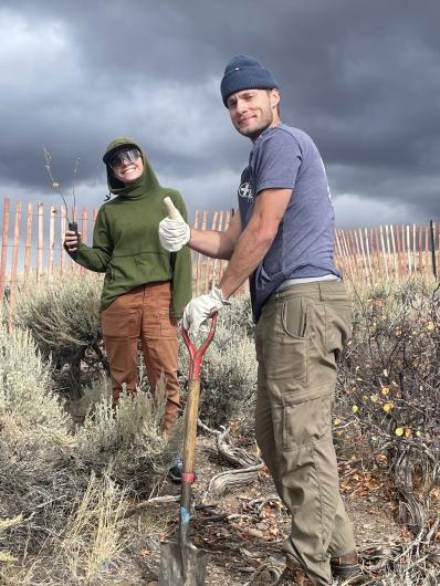 A woman holds up a seedling while a man gives the thumbs-up sign