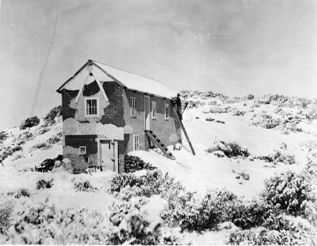 a long two-story building in the snow. a man stands on a ladder doing something to the roof.