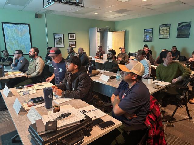 A room full of trainees sitting at tables observing a presentation.