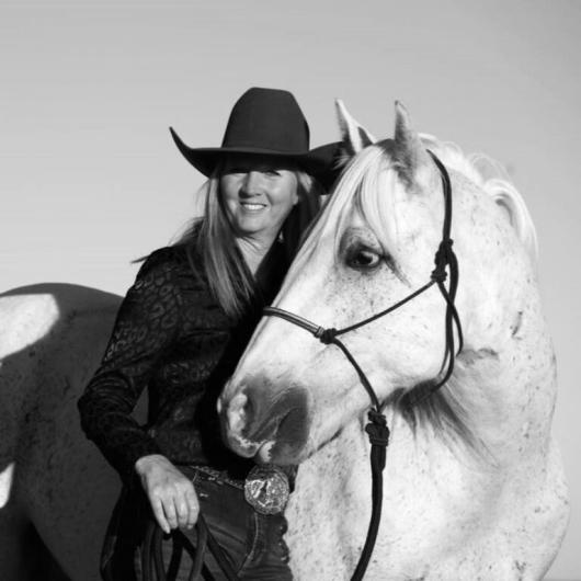 Woman in hat stands with light colored horse