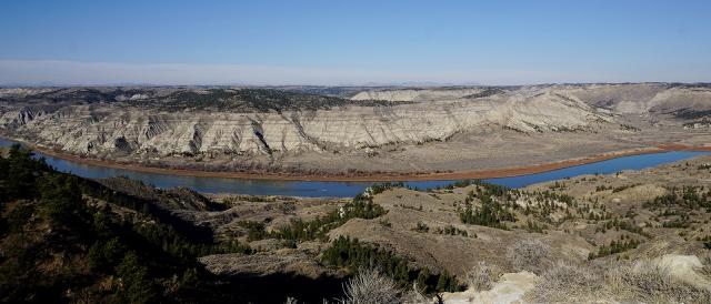 Wide panoramic view of a winding river cutting through arid, rocky hills under a clear blue sky.