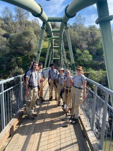 A group of six youth stand on a suspension bridge.