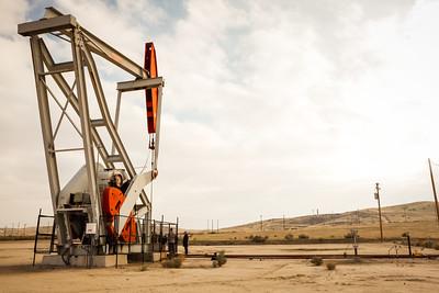 A white and red pump jack rises over dried grass hills.