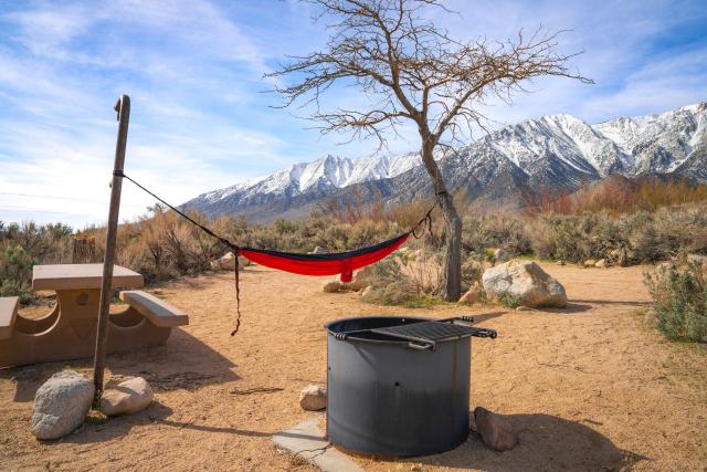 desery campground with a fire pit and hammock and snow capped mountains in the distance