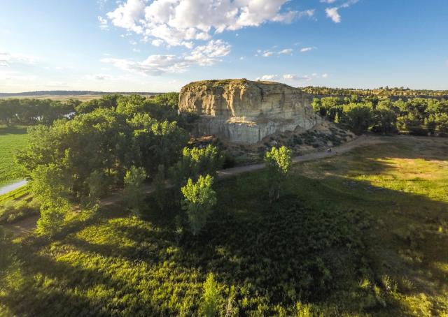 Aerial view if a large rock formation surrounded by green trees and a path along one side.