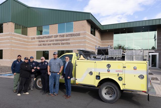 Group of people stand in front of a yellow fire engine, looking at the camera and smiling. 