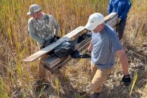 BLM volunteers carry a stack of lumber through tall grass