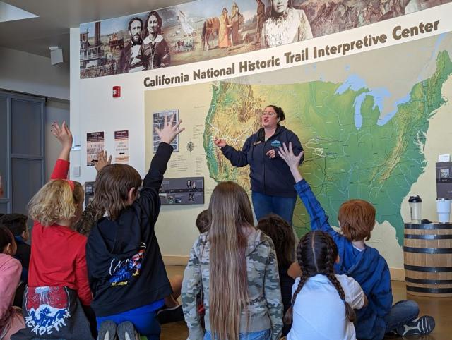 Students raise their hands to be called on by an educator in front of a map of the Oregon Trail