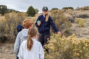 Ranger pointing at sage brush while children stand nearby