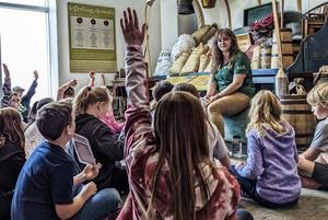 Students raising hands during a program with a ranger in front of replica covered wagon