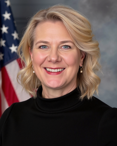 smiling person wearing a black shirt posing in front of a flag