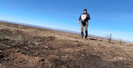 A BLM wildlife biologist uses a seed spreader to broadcast seeds.