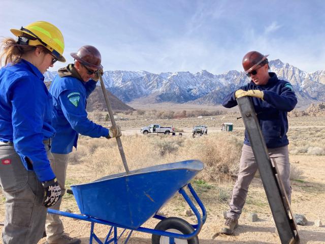 BLM workers near a blue wheelborrow and big granite mountains in the distance