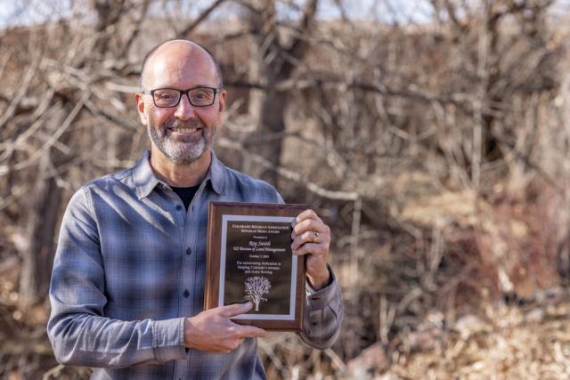 A man holds a placard in a field with trees in the background