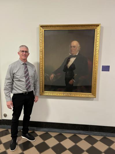 Collin Ewing poses next to a photo of his great-great-great-great-great uncle Thomas Ewing Sr. at the Main Interior Building in D.C. 