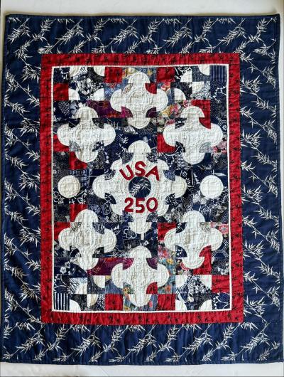 Patchwork quilt with red, white, and blue fabric, floral and geometric patterns, and "USA 250" stitched in the center.