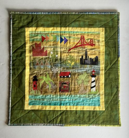 Quilt with colorful appliqué designs including a suspension bridge, city skyline, lighthouses, palm tree, windmill, and geometric shapes.