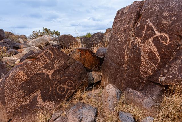 Various petroglyphs on boulders on a cloudy day.