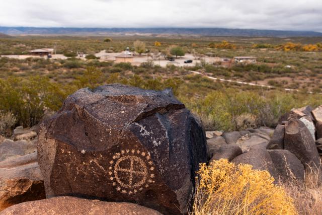  A petroglyph in the foreground on a hill and a building for visitors in the lower distance. 
