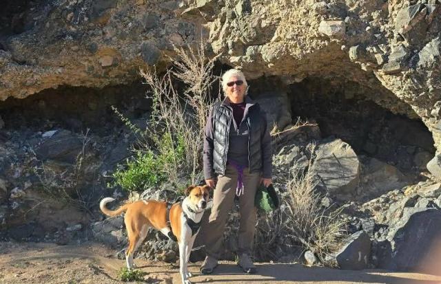 Volunteer poses with her dog in front of a rock formation on a walk.