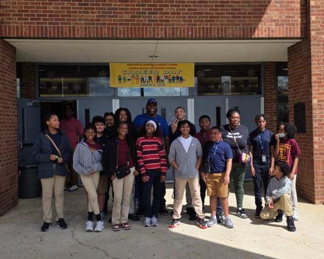 Group of students and adults posing outside a school entrance under a "Career Day" banner dated March 6, 2020.