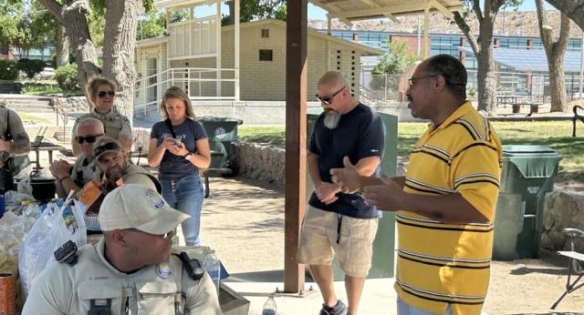 Several Bureau of Land Management staff members gather under a shaded pavilion while a man in a yellow striped shirt speaks to the group during an outdoor employee event.