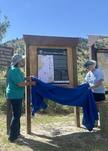 Two people unveil a new informational kiosk by removing a blue cloth