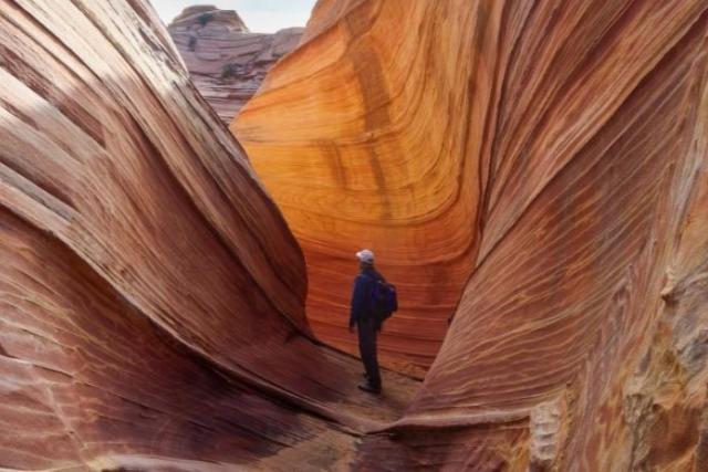 Hiker in orange and pink sandstone slot canyon