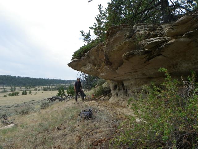 a man stands under a rocky outcrop