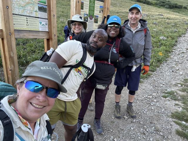Group selfie of five hikers in front of a trailhead sign