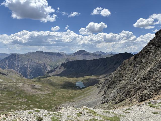A mountain view looking downward into an alpine tundra covered landscape with a small tarn