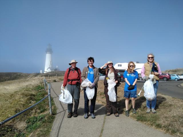 Group of people holding cleanup bags on a path near a foggy lighthouse.