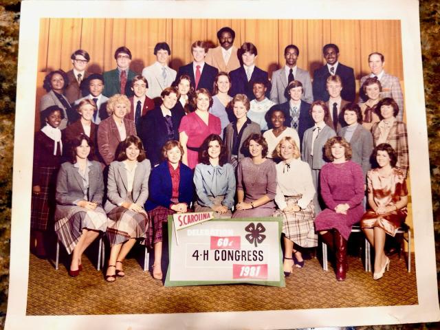 A vintage group photograph of a large delegation of young people and adults arranged in several rows. A sign in front reads “S. Carolina Delegation 4‑H Congress 1981.” The group is posed in front of a gold curtain, wearing late‑1970s and early‑1980s style clothing.