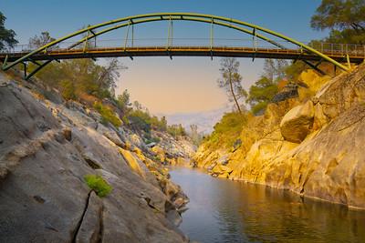 A large green bridge over a granite gorge at sunset