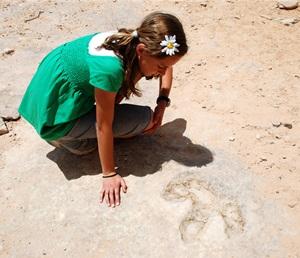 Young girl in green dress looks at dinosaur footprint in sandstone