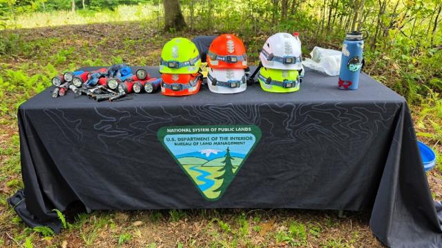 Safety helmets and headlamps used for the BLM Traveling Cave Display sit on a table branded with the Bureau of Land Management’s National System of Public Lands during Scouting America’s 2026 National Jamboree.