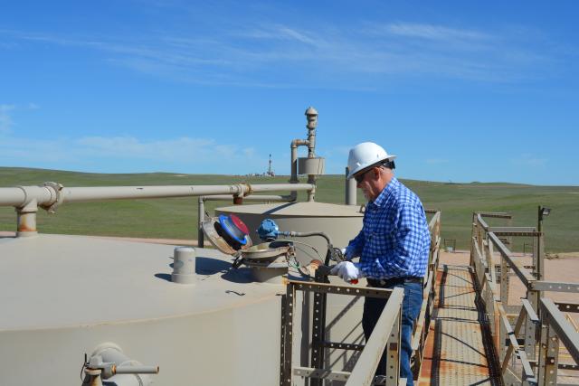 a man in a blue shirt and white hard hat inspects an opening in a metal structure