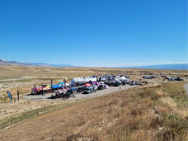 A gravel lot full of vans, tents, and bicycles in a hilly desert landscape 