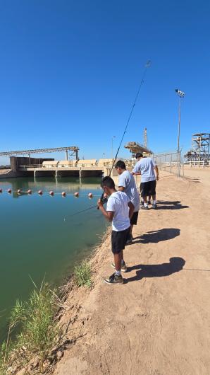 Three boys fishing with rods along a canal bank beside a dam, floats on the water