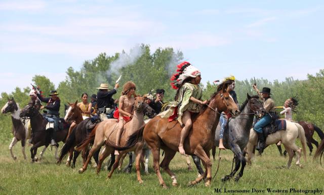 About a dozen horses and riders in action, appearing to reenact a battle between Union and American Indian forces
