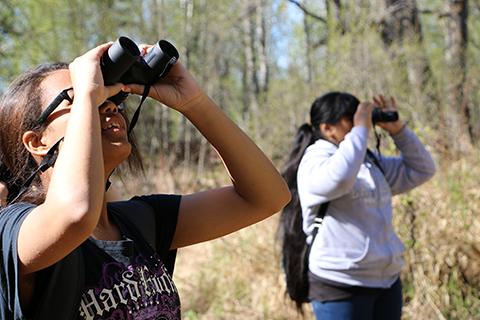 Two girls using binoculars to look up in the trees for birds at Campbell Tract