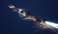 Cars and pickup trucks drive the Community Winter Access Trail snow road at night.