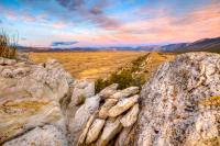 Rocks with the sunsetting and clouds in the distance overlooking a brown grass landscape.