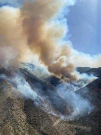 Smoke rises above rugged, mountainous terrain