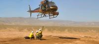 Helicopter hovering over the ground with three firefighters underneath.